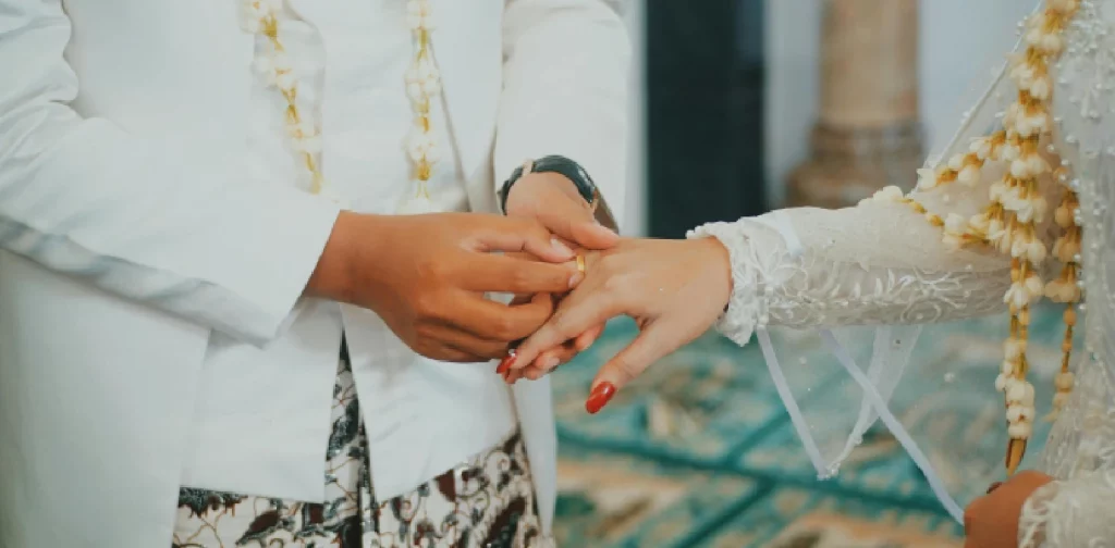 Pengantin pria sedang memasangkan cincin pada jari pengantin wanita