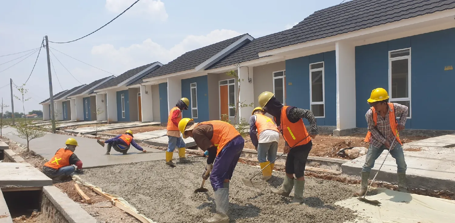 beberapa pekerja sedang mengaspal jalan di depan deretan rumah