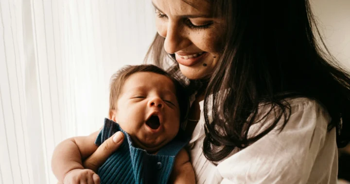 seorang perempuan dengan kemeja putih menggendong seorang bayi dengan baju biru