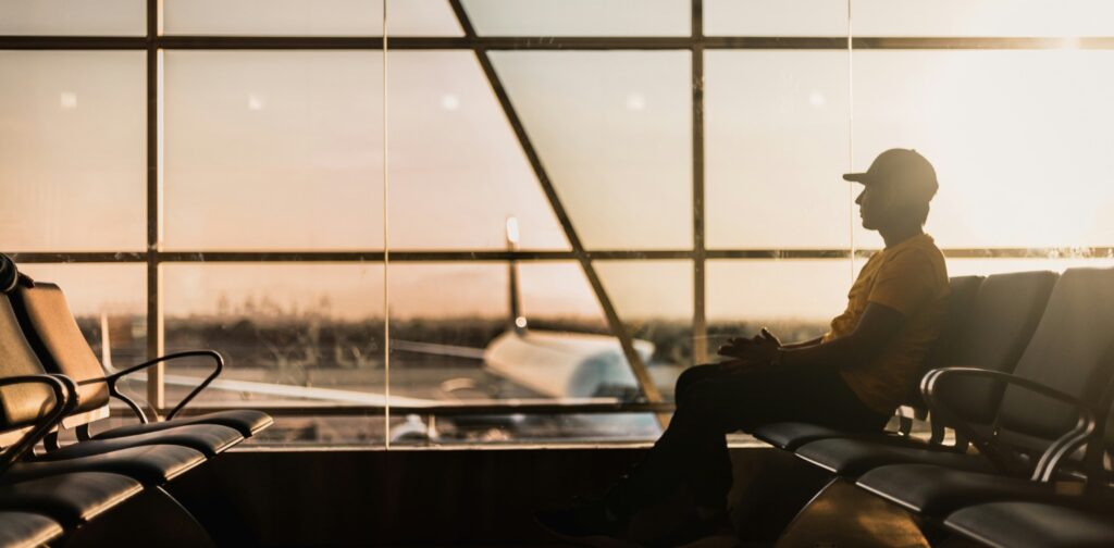seseorang duduk di kursi tunggu bandara di dekat jendela kaca