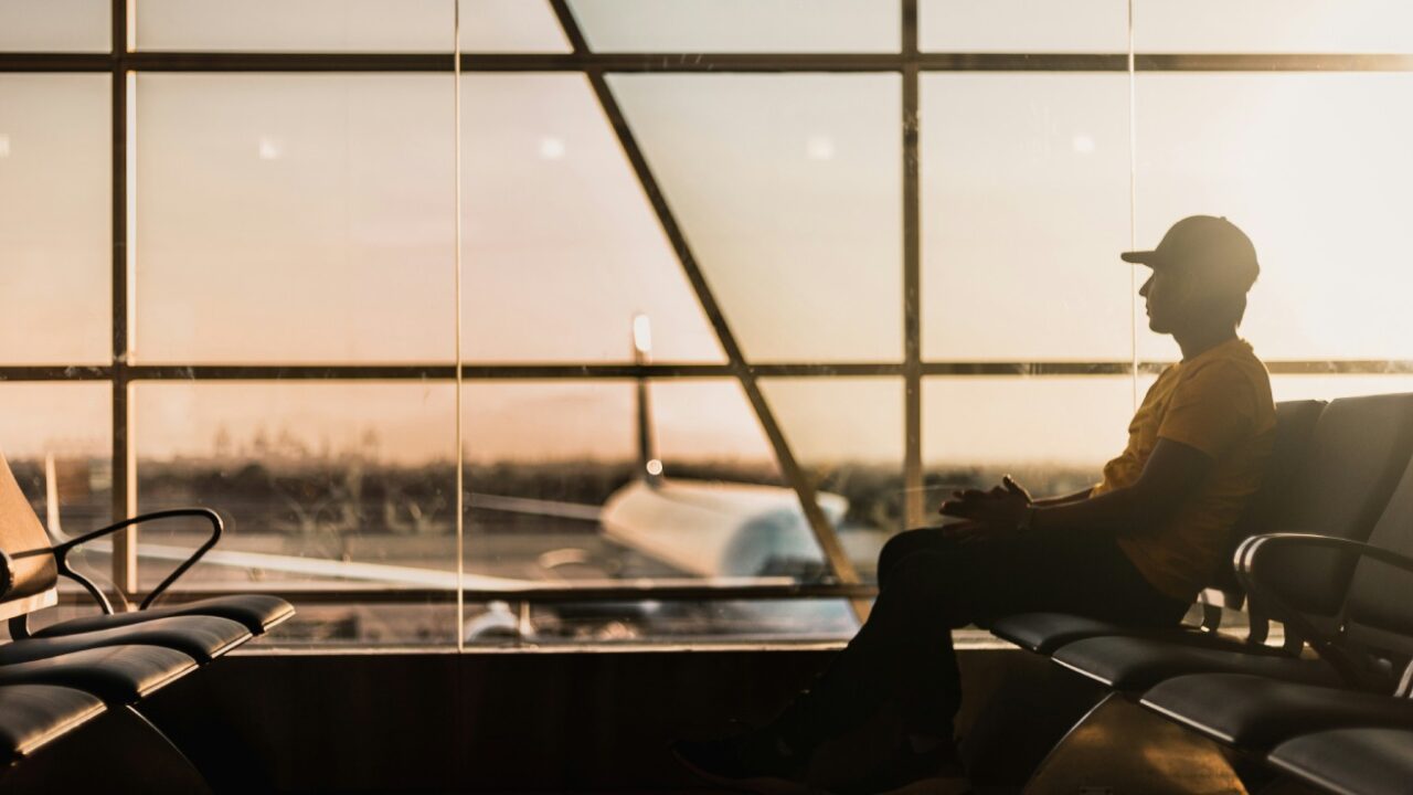 seseorang duduk di kursi tunggu bandara di dekat jendela kaca
