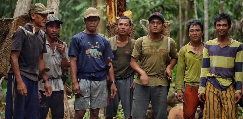 tujuh orang berdiri bersisian di hutan dengan beberapa memanggul kayu