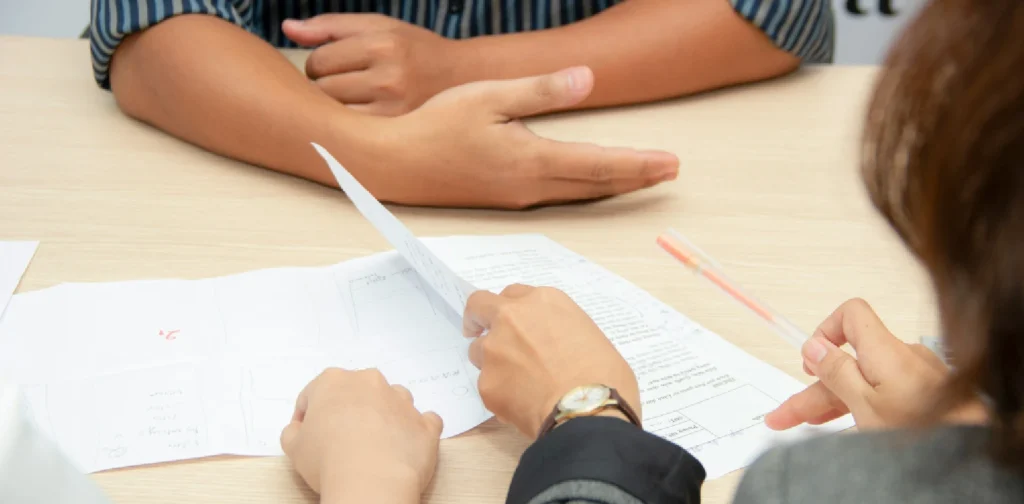 lembaran resume di meja dengan tampak close up tiga orang yang saling berhadapan