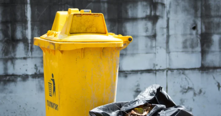 tempat sampah berwarna kuning dengan kantong plastik berisi sampah di sebelahnya