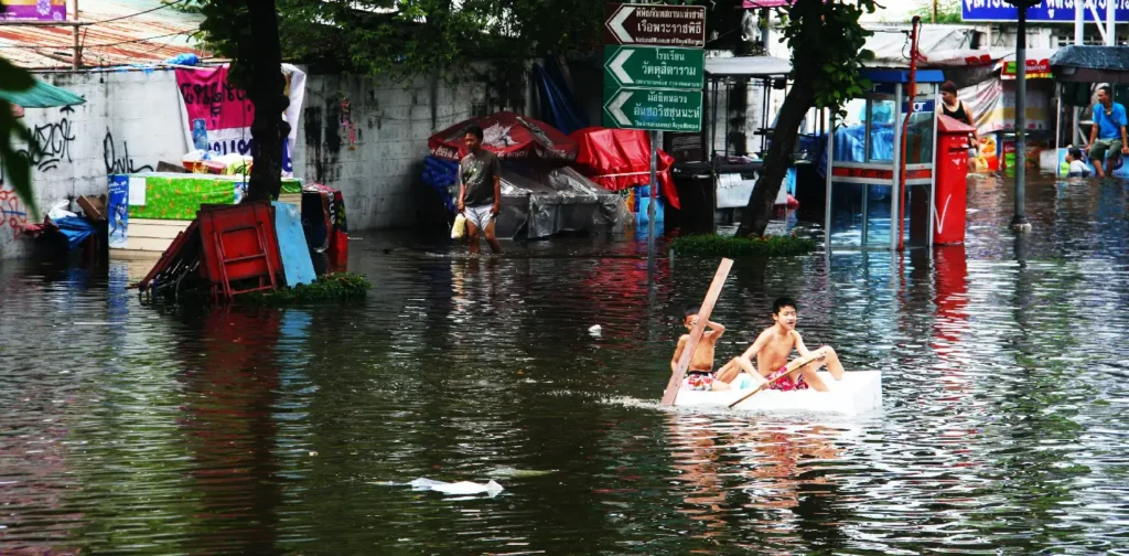 dua anak lelaki di perahu kayu kecil sedang mendayung di tengah jalanan penuh air banjir