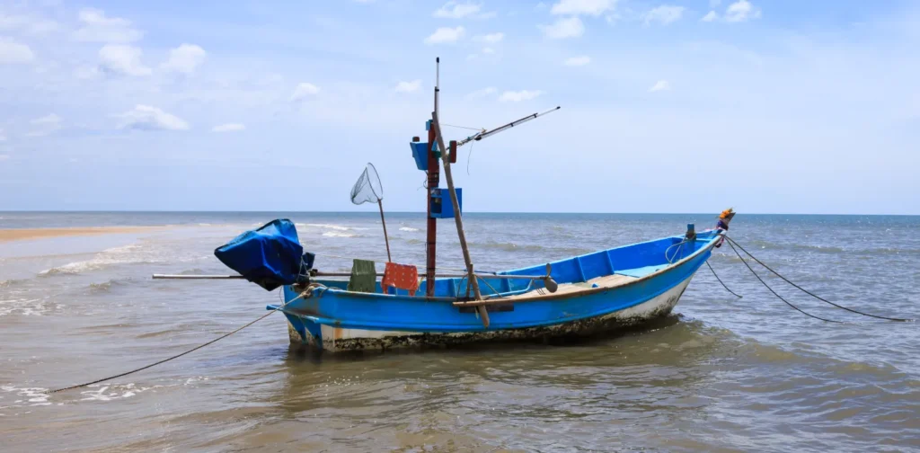 sebuah kapal nelayan berwarna biru dan putih berada di laut dengan latar belakang langit biru cerah