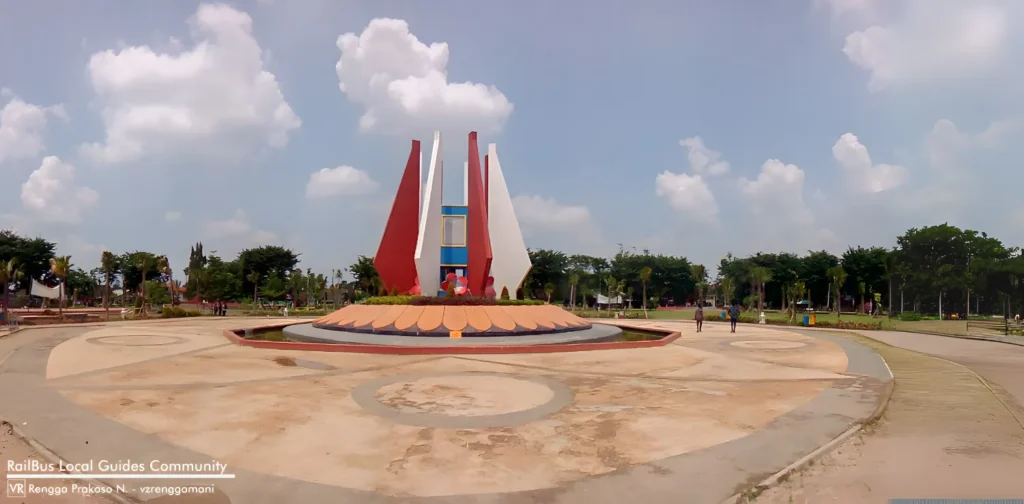 Monumen Alun-alun Mojokerto dikelilingi oleh taman hijau dengan langit biru yang cerah sebagai latar belakang.