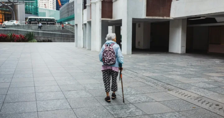 seorang perempuan tua berjalan di jalan dengan tongkat, dengan punggung membelakangi kamera