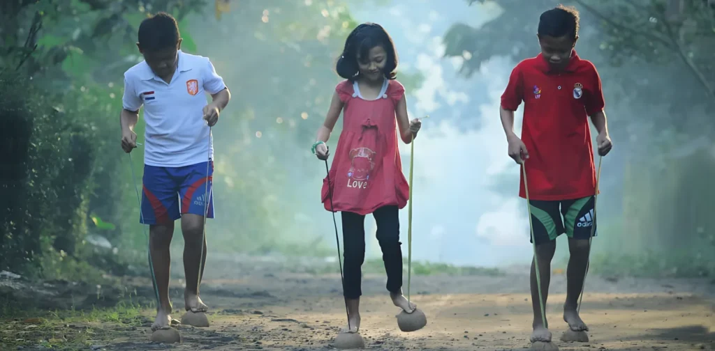 dua anak laki-laki dan seorang anak perempuan di tengah bermain engklek.