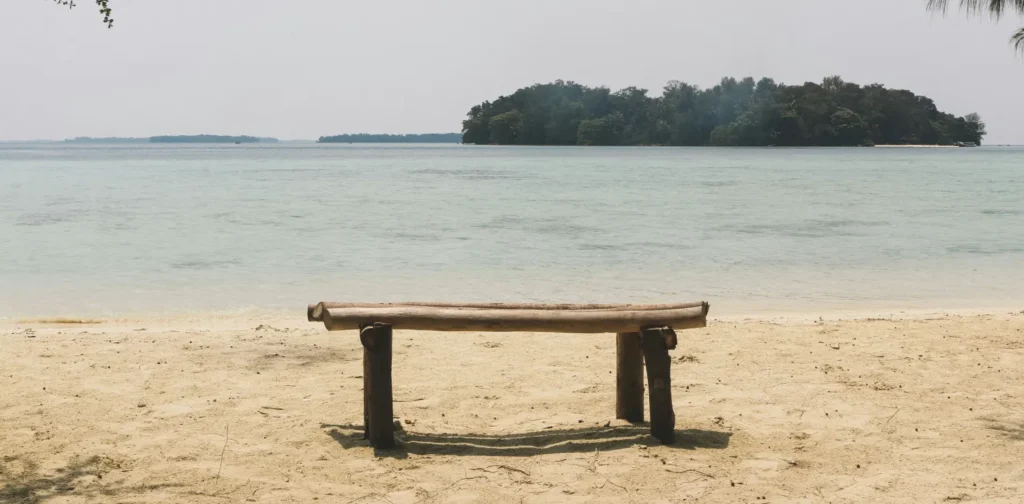 Bangku kayu di tepi pantai dengan pulau-pulau kecil di tengah laut.