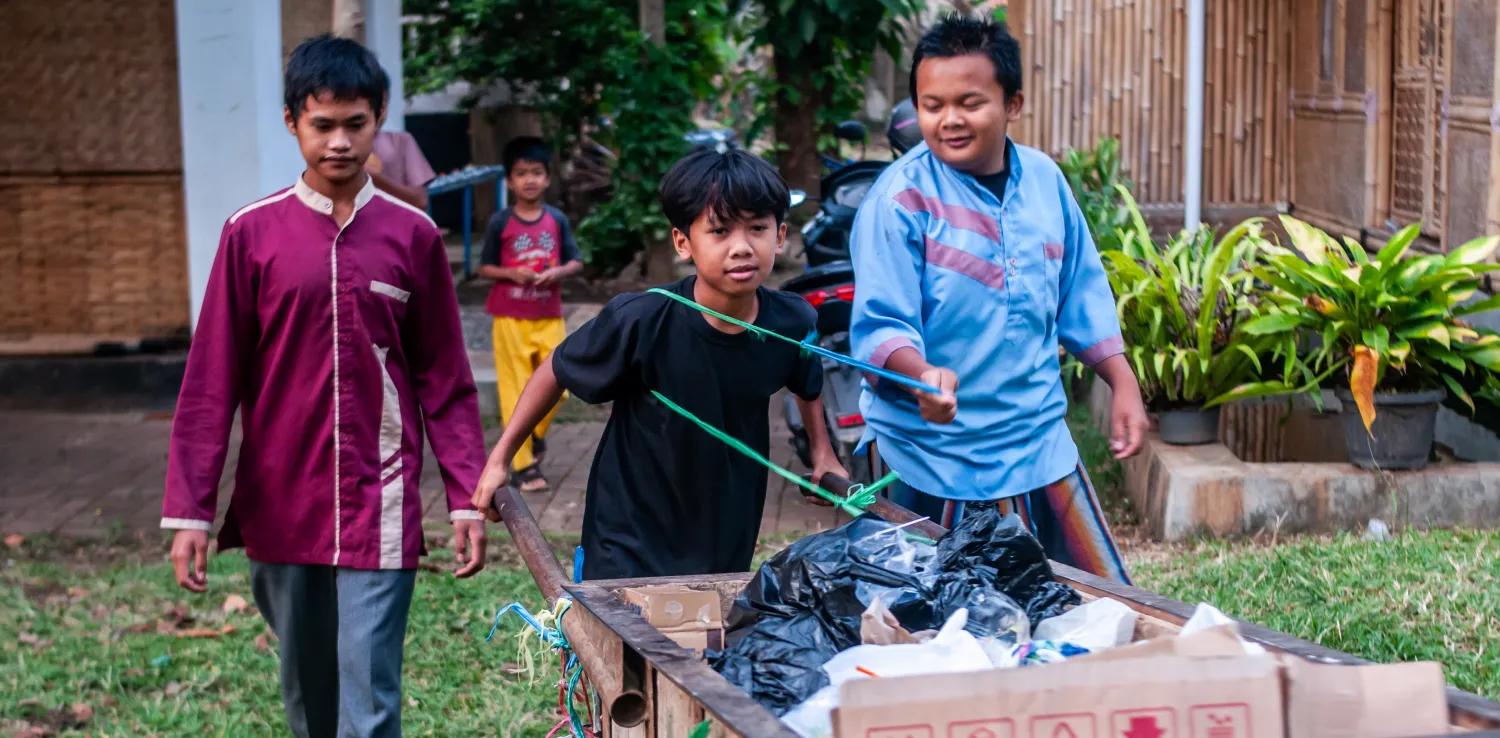 4 orang anak mendorong gerobak sampah.