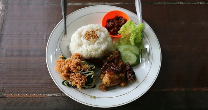 piring makan berisi nasi dengan lauk ayam, urap, sambal, dan irisan timun dan selada