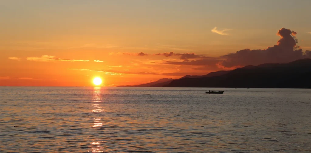 siluet sampan nelayan di laut dengan latar matahari terbenam di cakrawala