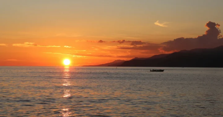 siluet sampan nelayan di laut dengan latar matahari terbenam di cakrawala