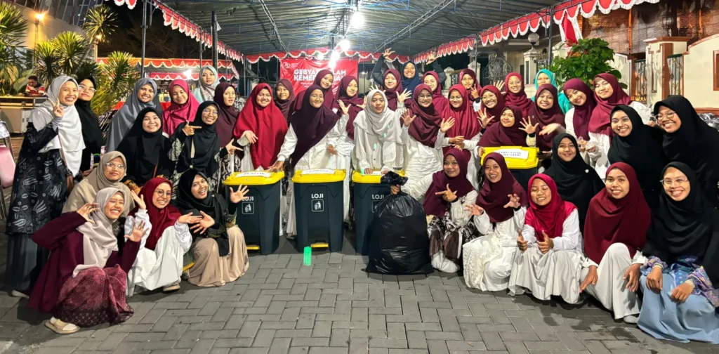 sekelompok perempuan berhijab berfoto bersama di bawah atap dengan keranjang dan plastik sampah di depan