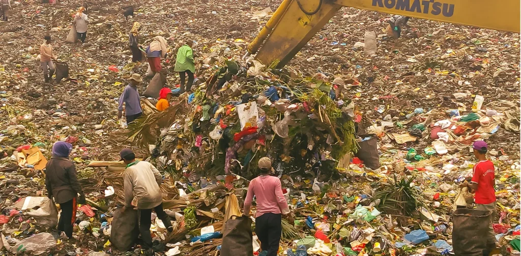 sekelompok pemulung mengumpulkan sampah di tempat pembuangan sampah akhir dengan alat pengeruk sampah berwarna kuning di tengah mereka