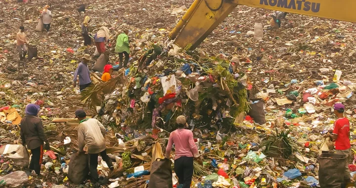 sekelompok pemulung mengumpulkan sampah di tempat pembuangan sampah akhir dengan alat pengeruk sampah berwarna kuning di tengah mereka