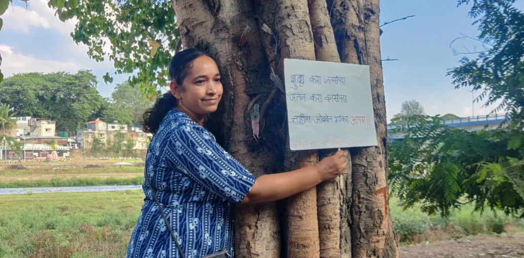 seorang perempuan memeluk pohon sambil memegang tanda untuk memprotes deforestasi dalam Gerakan Chipko.