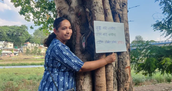 seorang perempuan memeluk pohon sambil memegang tanda untuk memprotes deforestasi dalam Gerakan Chipko.