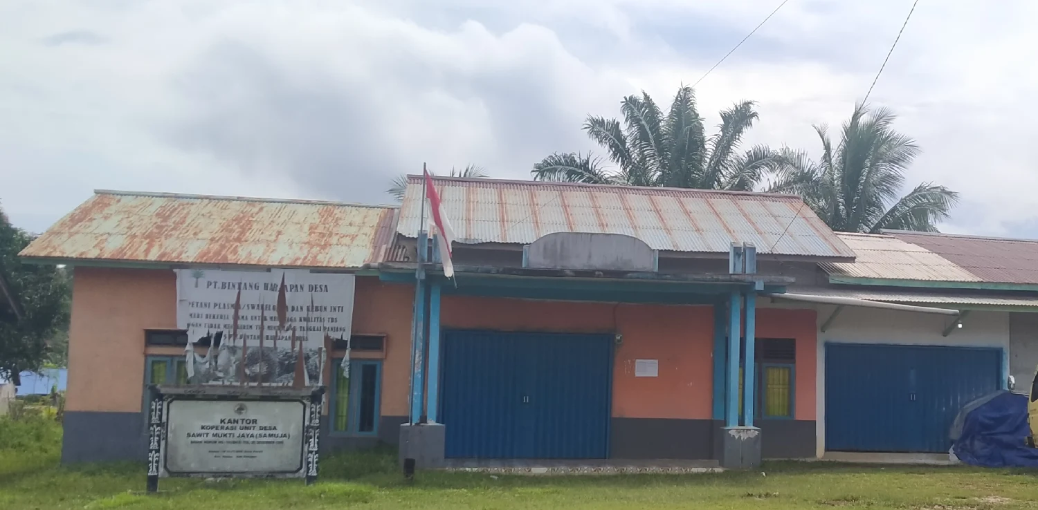 bangunan kantor koperasi dengan cat dominasi warna oranye dan pintu berwarna biru dengan tiang bendera di halaman depan