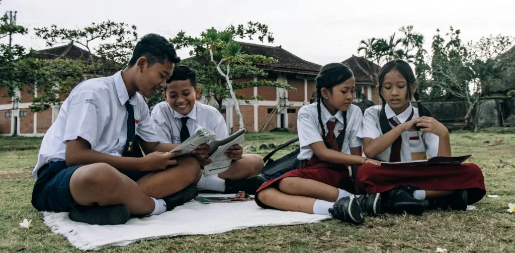 empat siswa mengenakan seragam sedang membaca buku di halaman