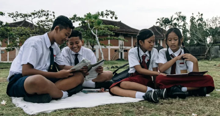empat siswa mengenakan seragam sedang membaca buku di halaman