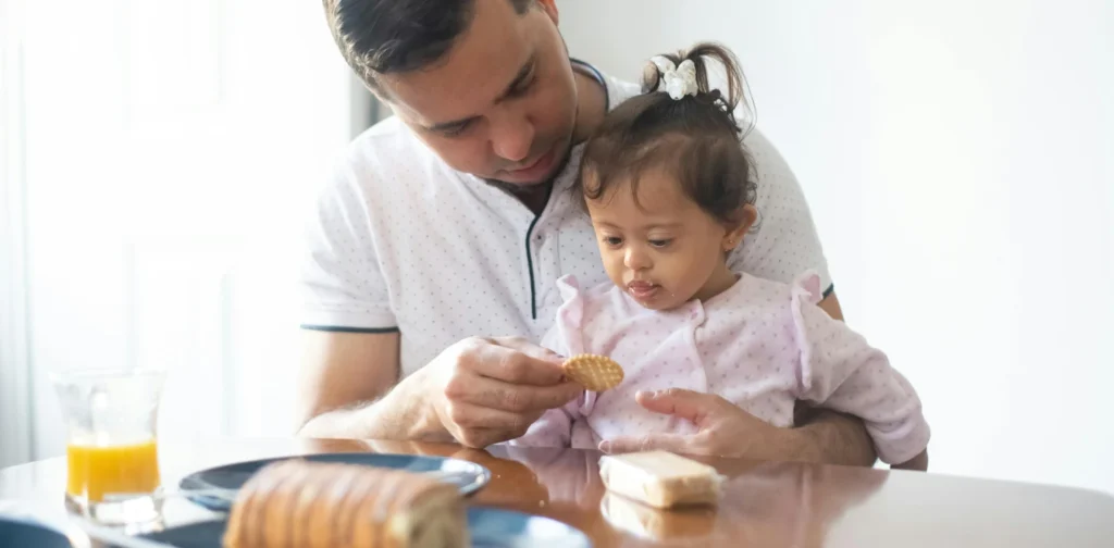 seorang ayah memberi makan anak perempuannya biskuit di meja makan
