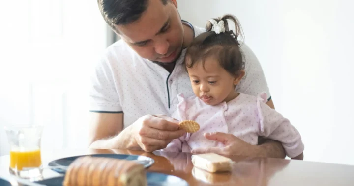seorang ayah memberi makan anak perempuannya biskuit di meja makan