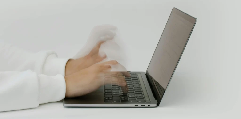 tampak samping tangan dengan tampilan yang buram sedang mengetik di laptop