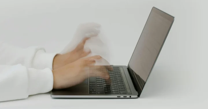 tampak samping tangan dengan tampilan yang buram sedang mengetik di laptop