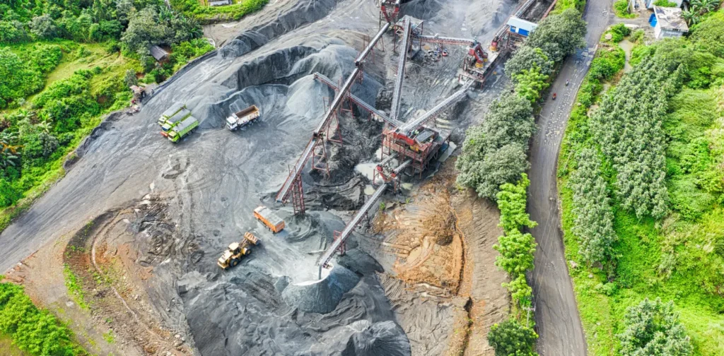 foto udara penambangan pasir dengan truk dan alat-alat berat yang dikelilingi oleh pepohonan