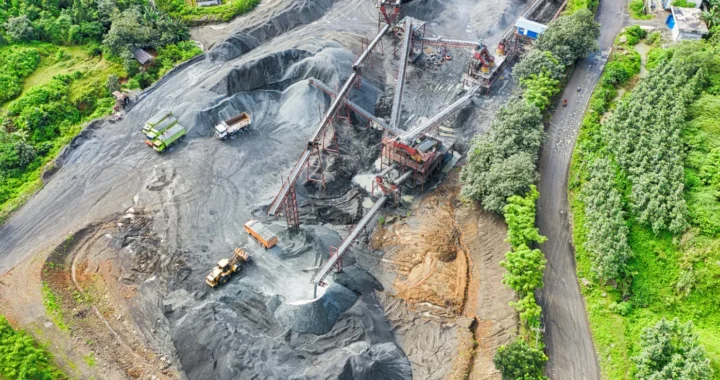 foto udara penambangan pasir dengan truk dan alat-alat berat yang dikelilingi oleh pepohonan