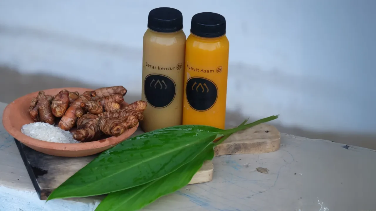 dua botol berisi jamu beras kencur dan kunyit asem serta rempah lainnya di atas talenan kayu
