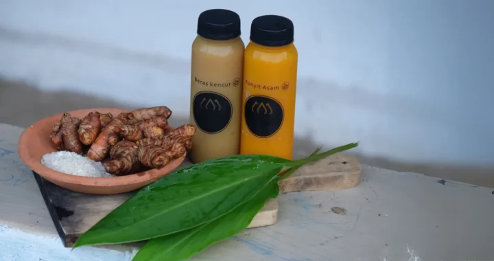 dua botol berisi jamu beras kencur dan kunyit asem serta rempah lainnya di atas talenan kayu