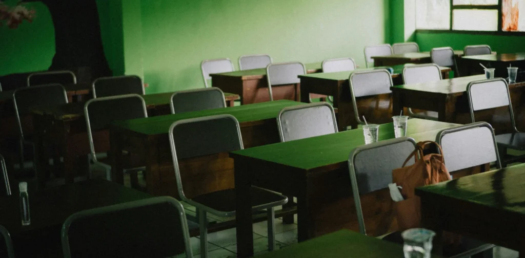 ruang kelas yang kosong dengan barisan rapi kursi dan meja dan tembok hijau