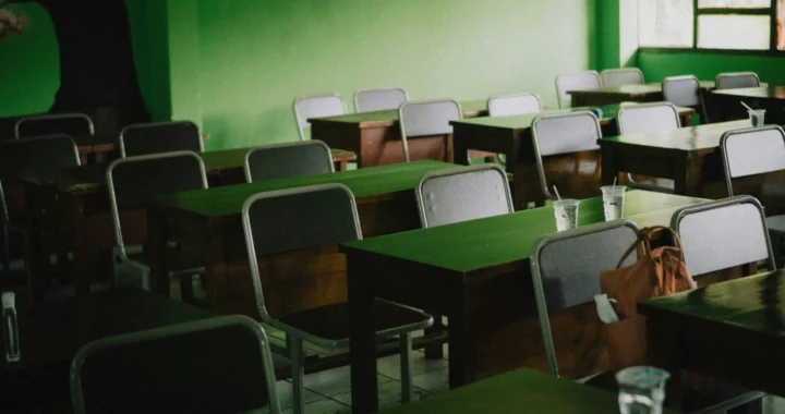 ruang kelas yang kosong dengan barisan rapi kursi dan meja dan tembok hijau