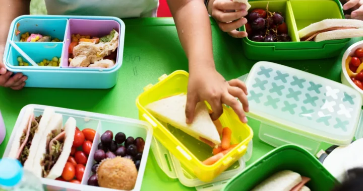Dua anak sedang memegang roti dengan banyak kotak bekal berisi buah dan berbagai makanan di hadapannya.
