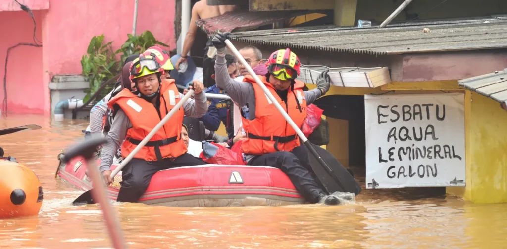 beberapa orang mendayung perahu di permukiman saat banjir.