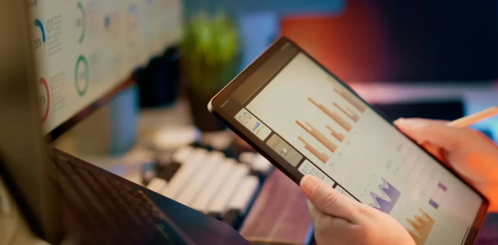 Seseorang menganalisis data keuangan pada tablet dan monitor