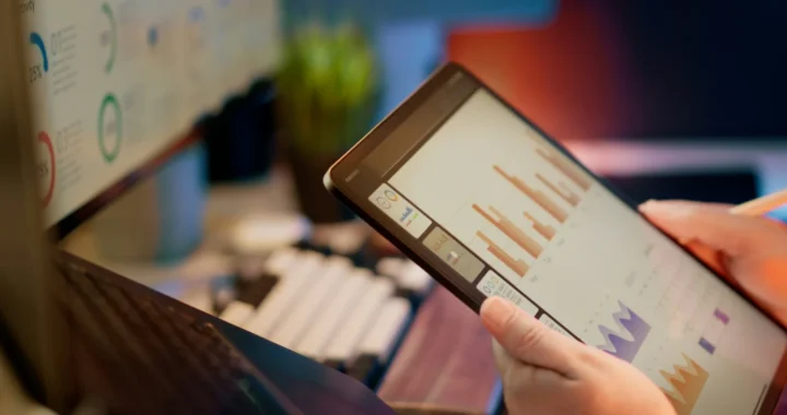 Seseorang menganalisis data keuangan pada tablet dan monitor
