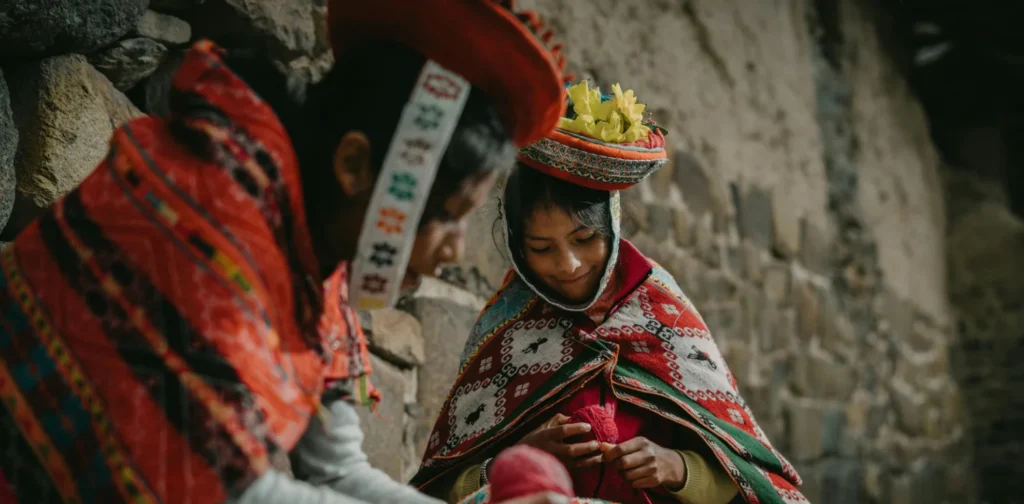 dua perempuan mengenakan pakaian tradisional Peru duduk di dekat dinding batu