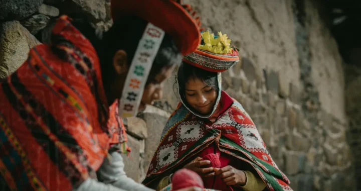 dua perempuan mengenakan pakaian tradisional Peru duduk di dekat dinding batu