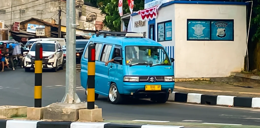 mobil angkutan berwarna biru tanpa penanda rute di kelokan jalan dekat pos polisi lalu lintas