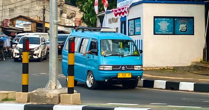 mobil angkutan berwarna biru tanpa penanda rute di kelokan jalan dekat pos polisi lalu lintas