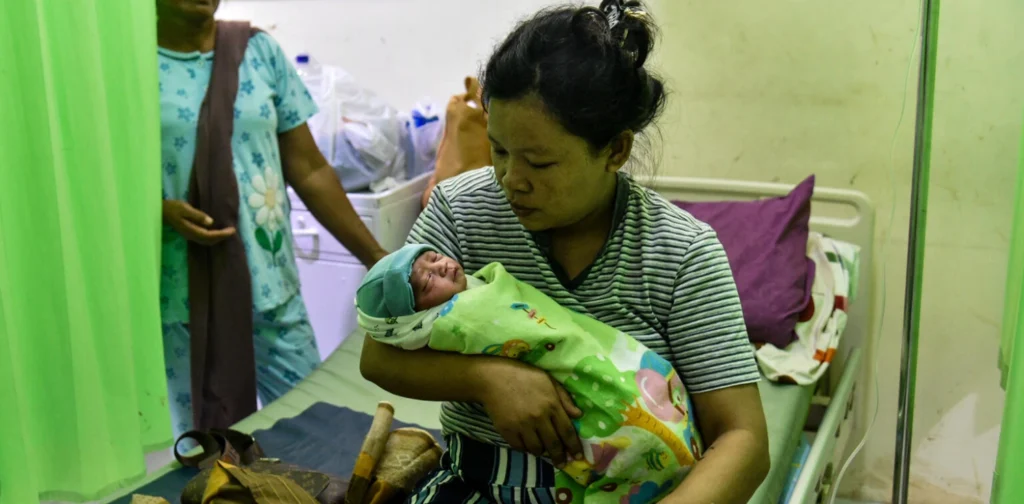 seorang ibu menggendong bayi di atas kasur tempat tidur