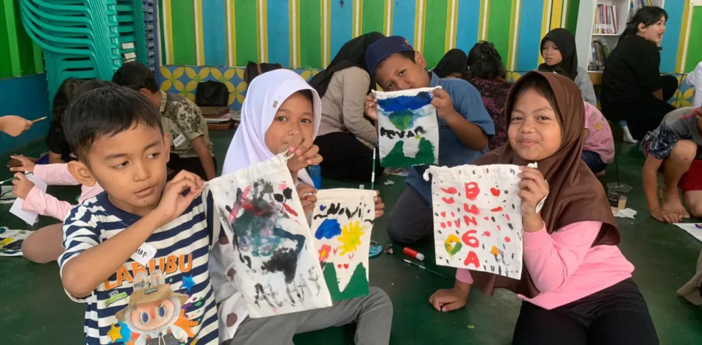 Empat anak dalam acara literasi Inisiasi Lantara berpose di depan kamera sambil menunjukkan pouch buku hasil lukisan mereka sendiri.