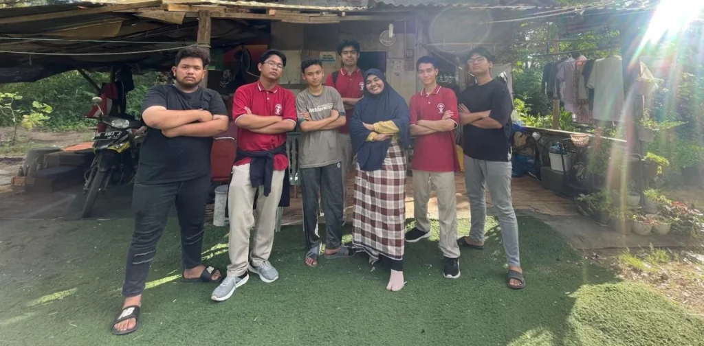 Sekelompok laki-laki muda berfoto bersama seorang ibu di depan sebuah rumah.