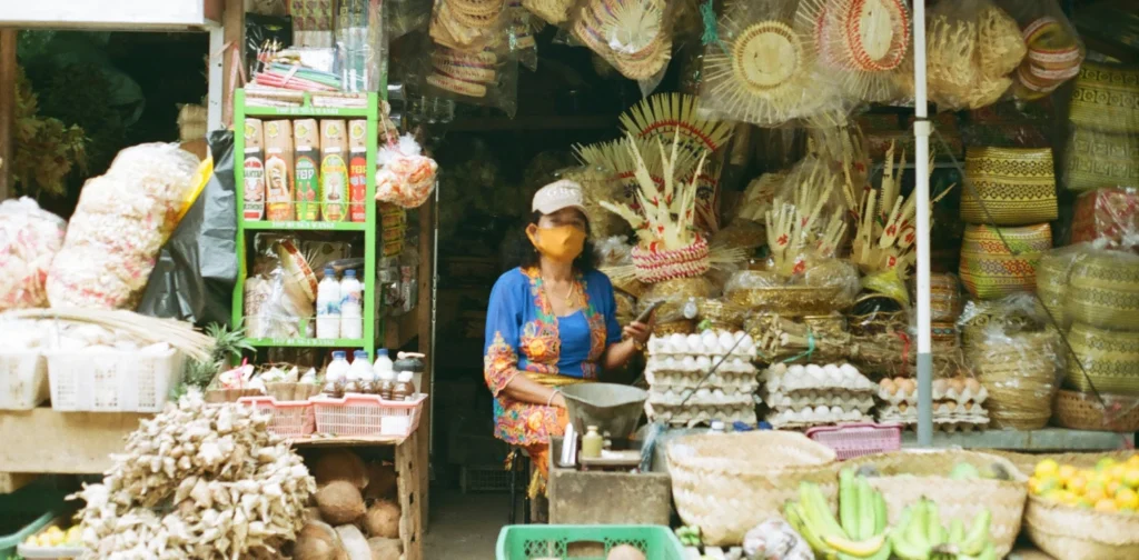 seorang perempuan dengan baju biru duduk di depan toko dengan barang-barang anyaman bambu di sekelilingnya