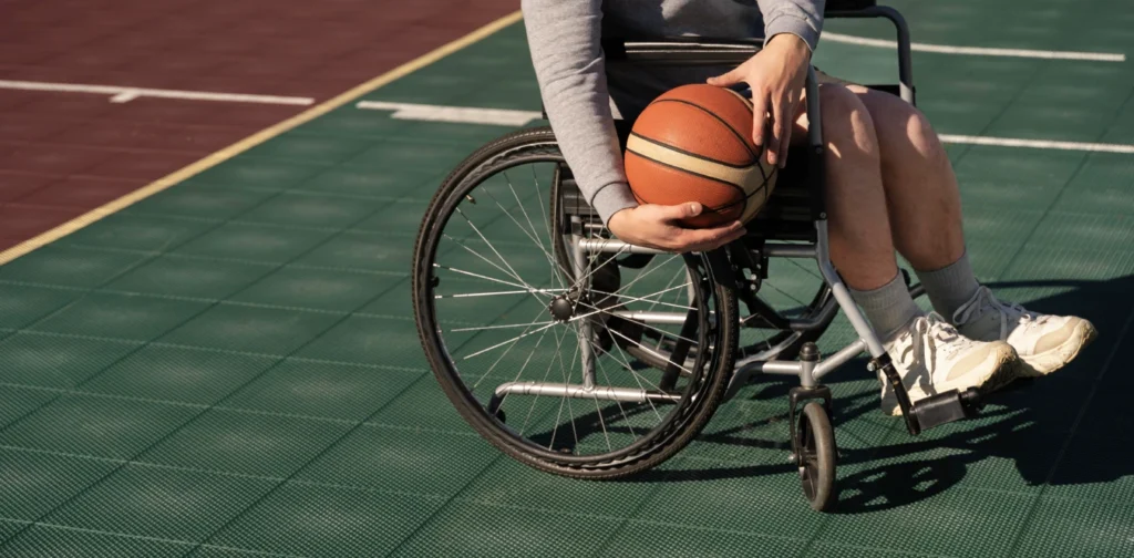 Seorang penyandang disabilitas di kursi roda sedang memegang bola basket di lapangan.