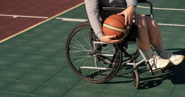 Seorang penyandang disabilitas di kursi roda sedang memegang bola basket di lapangan.